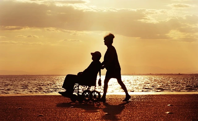 Persona in sedia a rotelle accompagnata sul lungomare al tramonto